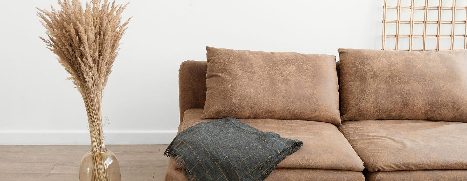 living room with a throw on a couch beside a large floor vase with a plant in it